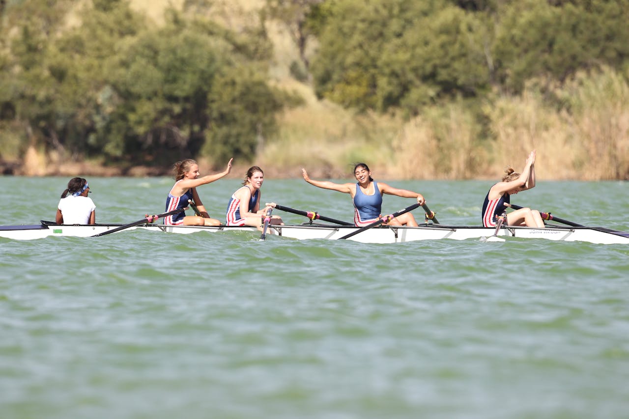A womens rowing team celebrates with high fives during a competition on a river under the daylight.
