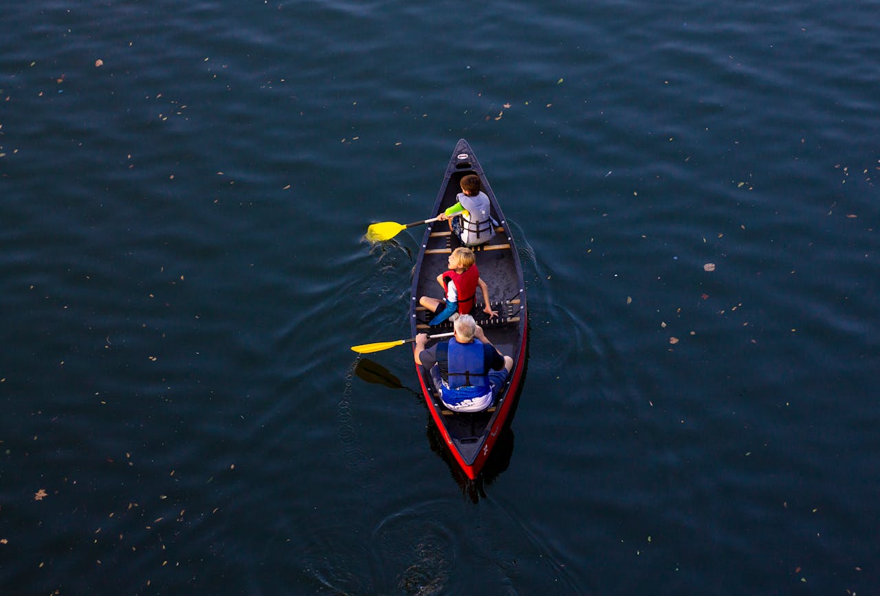 Grandparent and grandchildren enjoying a canoe ride on a serene lake under the sun.