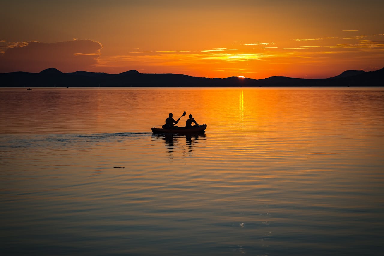 Silhouetted canoe with two people rowing on a calm lake at sunset, creating a serene and picturesque scene.